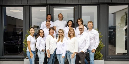 Die Menschen in der Gruppe zeigen eine freundliche Atmosphäre, während sie vor der Eingangstür eines Unternehmens posieren.