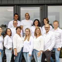 Die Menschen in der Gruppe zeigen eine freundliche Atmosphäre, während sie vor der Eingangstür eines Unternehmens posieren.