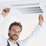 Ein Mann mit Vollbart hält ein Lüftungsgitter an der Decke
