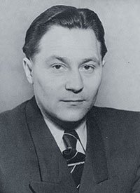 Ein Mann mit dunklem Haar und einem Anzug, der ernst in die Kamera schaut, mit einem neutralen Gesichtsausdruck.