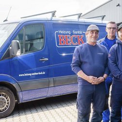 Die vier Männer in blauen Arbeitskleidung posieren stolz vor ihrem Firmenfahrzeug, das für Heizungs- und Sanitärdienstleistungen steht.