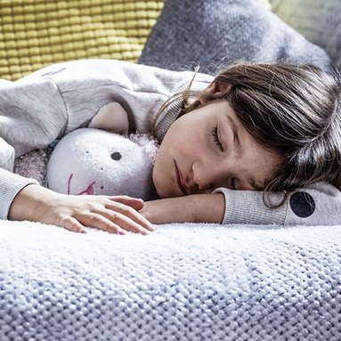 Ein Maedchen mit einem Kuscheltier im Arm, schlaeft