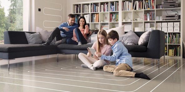 Eine Familie sitzt in einem Wohnzimmer mit einer Flaechenheizung, die beiden Kinder sitzten auf dem Boden