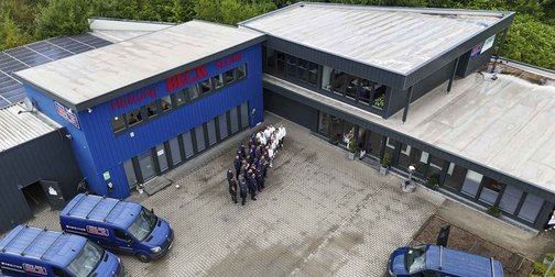 Eine Gruppe von Mitarbeitern steht vor einem modernen Gebäude mit blauer Fassade und Solarpanelen auf dem Dach.