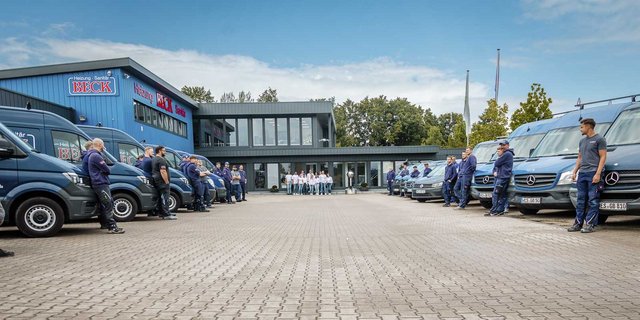 Eine Gruppe von Mitarbeitern steht in Uniform vor einem modernen Gebäude mit mehreren Lieferwagen, die bereit für den Einsatz sind.