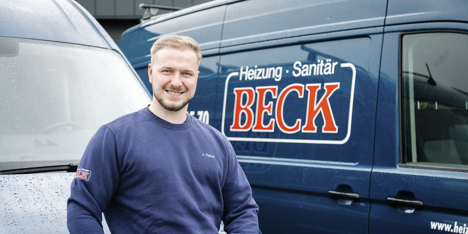 Ein junger Mann mit einem freundlichen Lächeln steht vor einem blauen Lieferwagen mit dem Logo 'BECK' darauf.