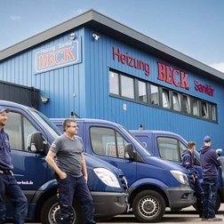 Eine Gruppe von Handwerkern steht entspannt vor einem blauen Gebäude mit dem Schriftzug 'Heizung Beck'.
