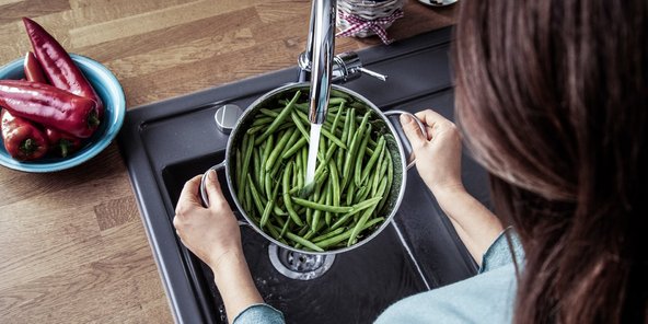 Eine Frau die die ein Topf mit Bohnen unter dem Wasser abspuehlt